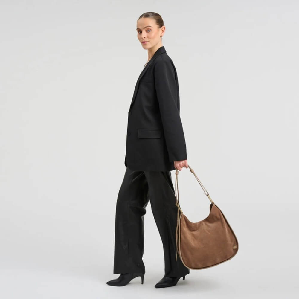 Person wearing a black suit holding a brown leather Depeche bag on a plain background