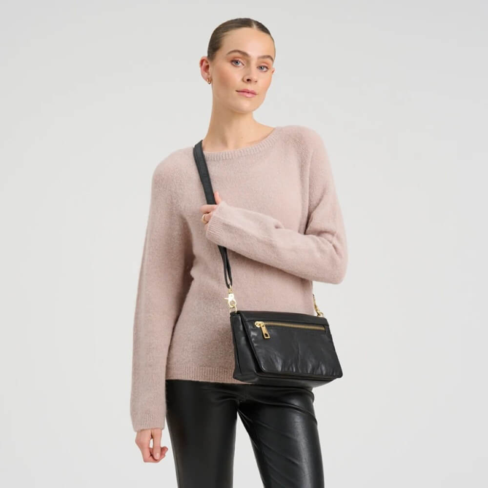 Woman holding a Depeche black leather handbag against a plain background