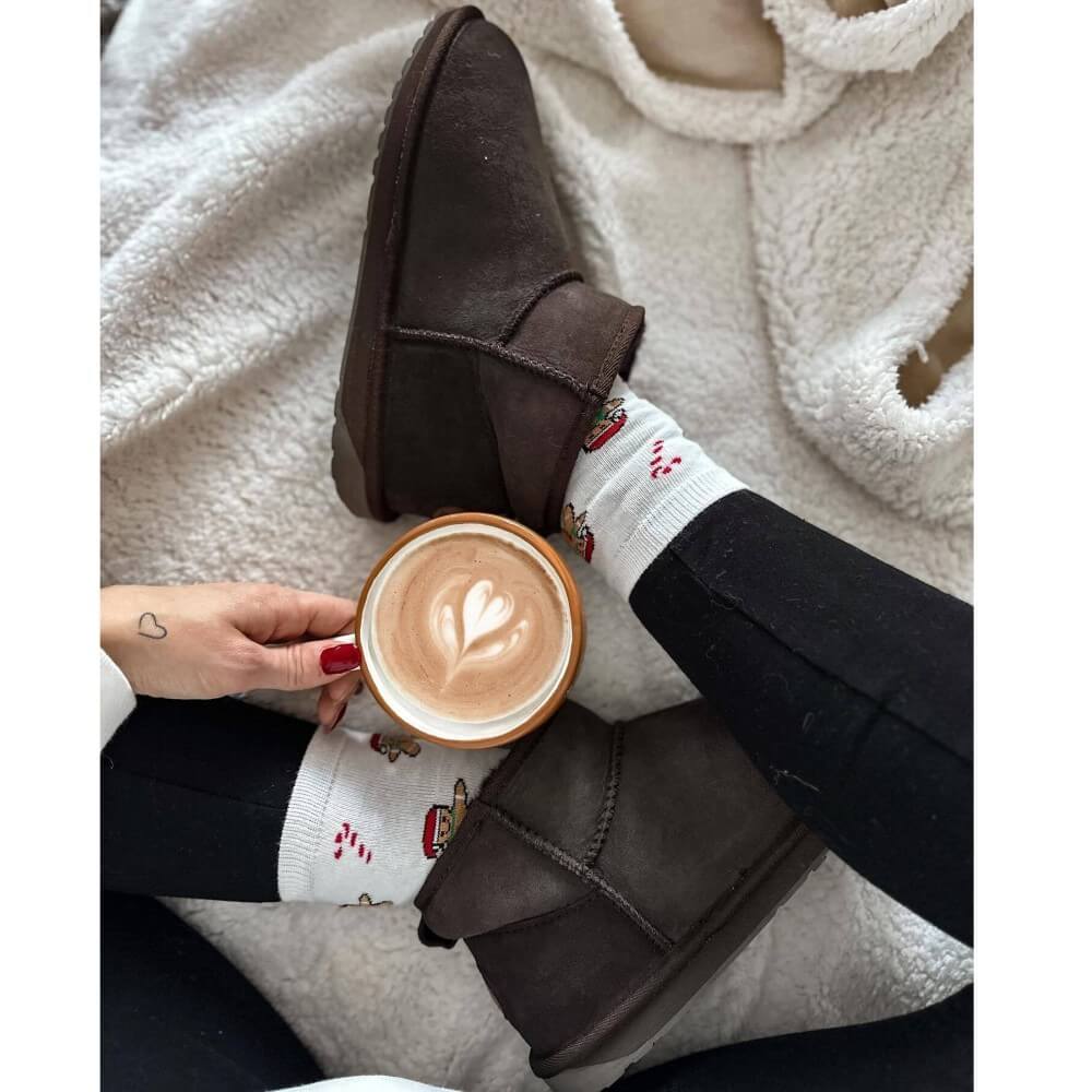 Person wearing brown slippers and holding a cup of coffee on a soft surface EMU Stinger Micro Chocolate