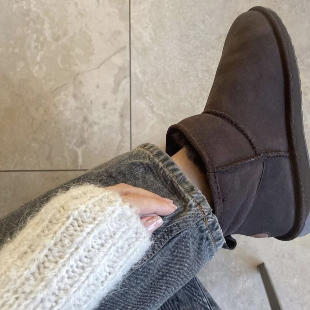 Brown suede shoe worn with a white sweater and blue jeans on a tiled  EMU Stinger Micro Chocolatefloor.