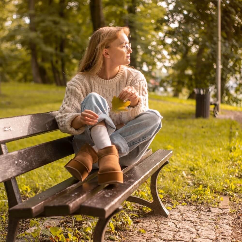 Woman sitting on a bench in a park holding a leaf EMU Stinger Micro Flatform Chestnut