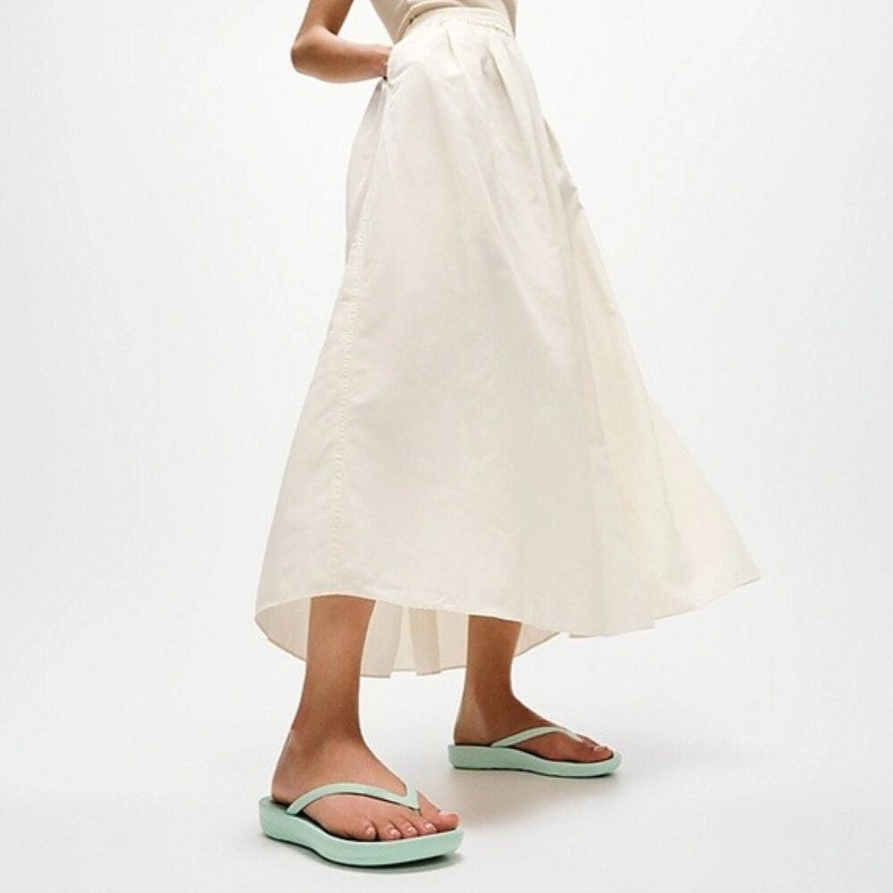 Person wearing a white skirt and light green sandals on a white background
