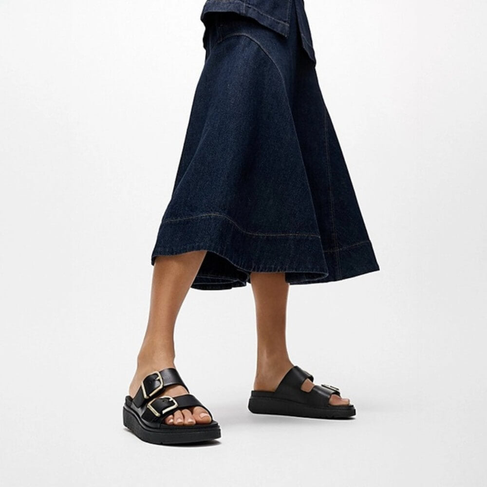 Person wearing a dark blue denim skirt and Fitflop black sandals on a white background