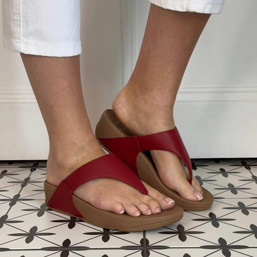 Fitflop Red and brown sandals worn on feet standing on a patterned floor.