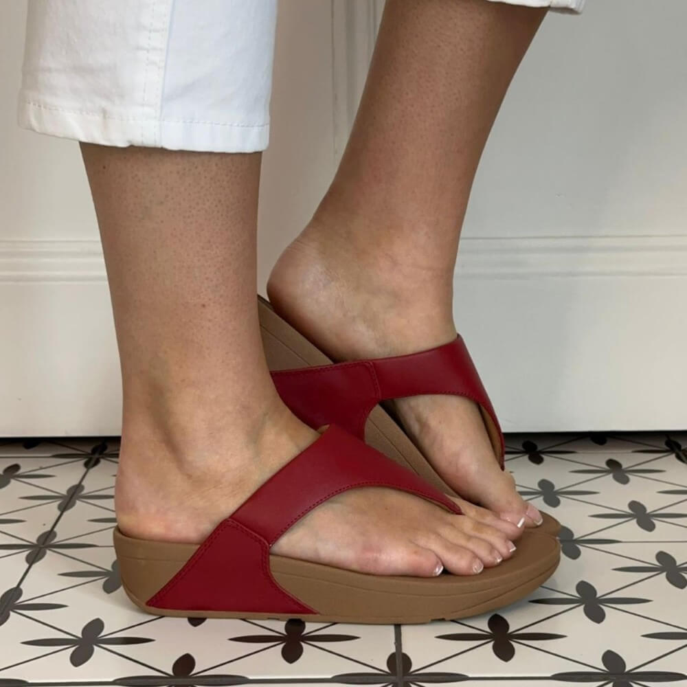 Fitflop Red sandals with brown soles worn by a person on a patterned floor.