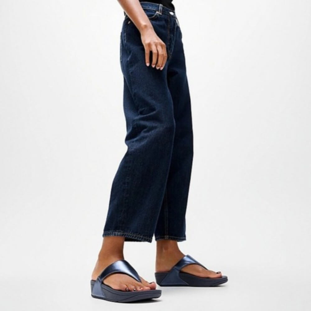 Person wearing dark blue jeans and Fitflop sandals on a light gray background
