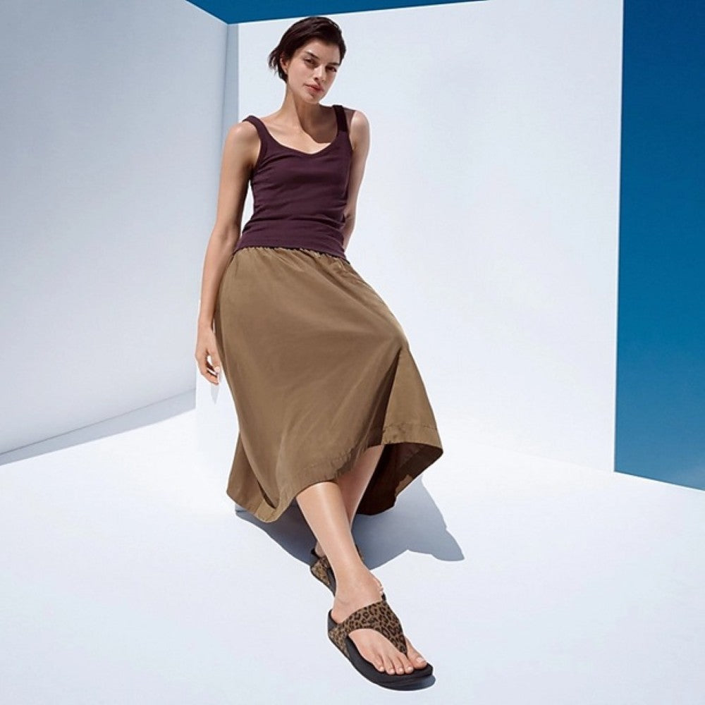 Woman wearing Leopard print Fitflops, brown tank top and beige skirt against a white and blue geometric background
