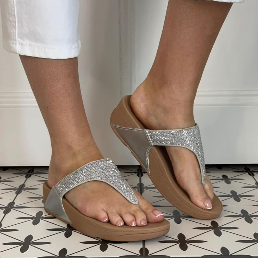 Fitflop silver sandals with glittery straps worn indoors on a patterned floor.