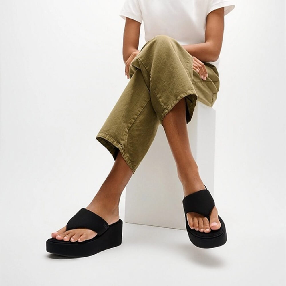 Person sitting wearing black fitfliops and brown trousers
