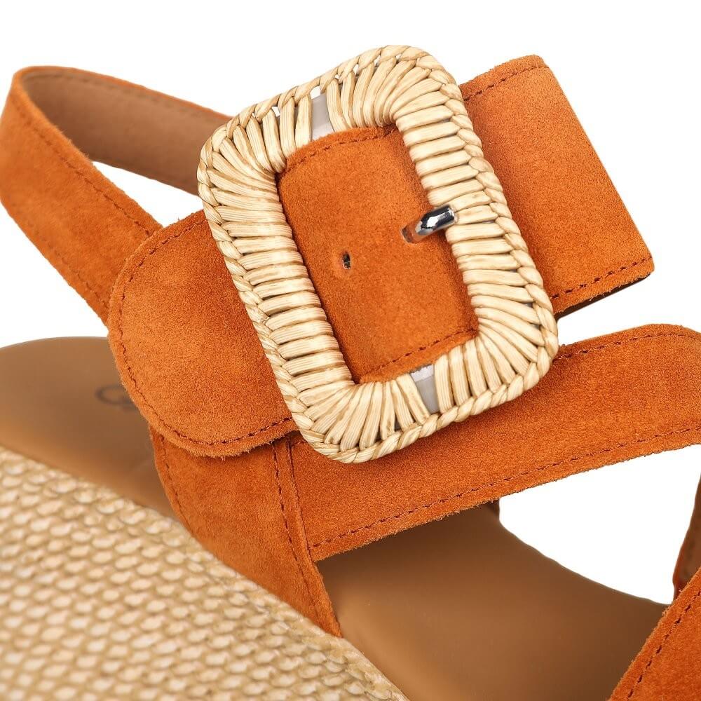 Close-up of an orange sandal with a woven strap buckle on a white background