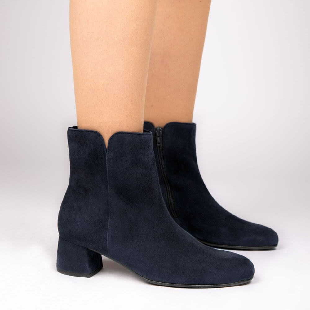 A pair of Gabor navy blue suede ankle boots with a low block heel and side zipper, shown on a model's feet against a light grey studio background.