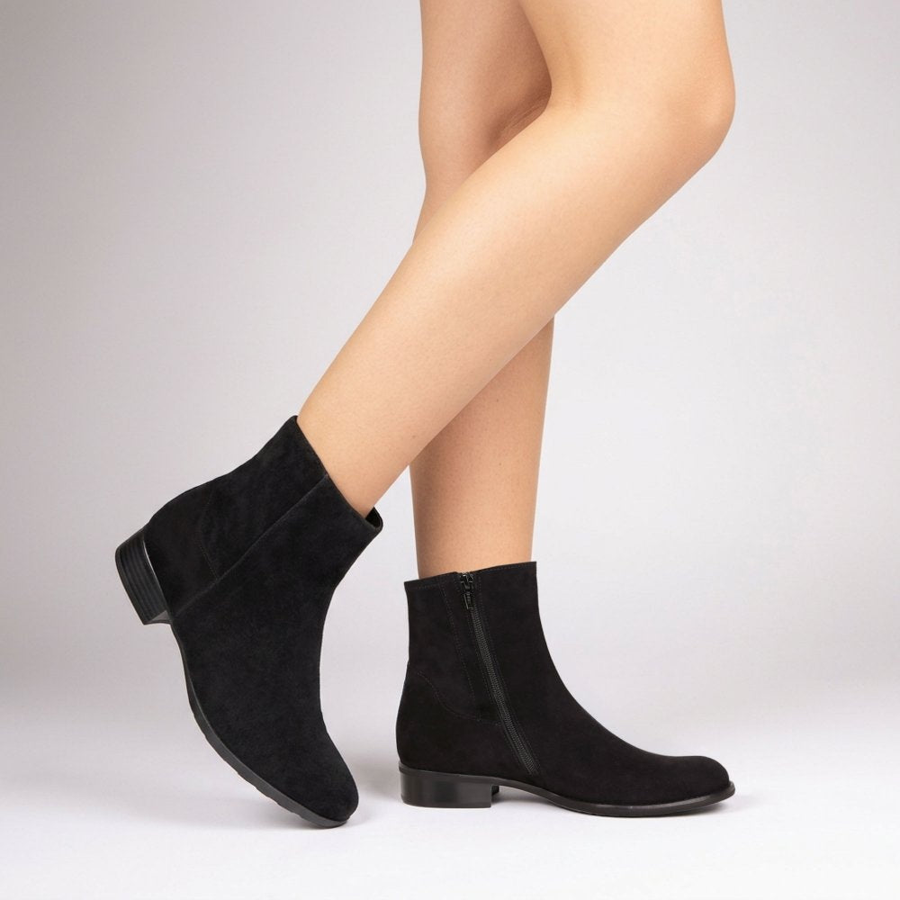 A pair of Gabor black suede ankle boots with low block heels, shown on a model's feet against a light grey studio background.