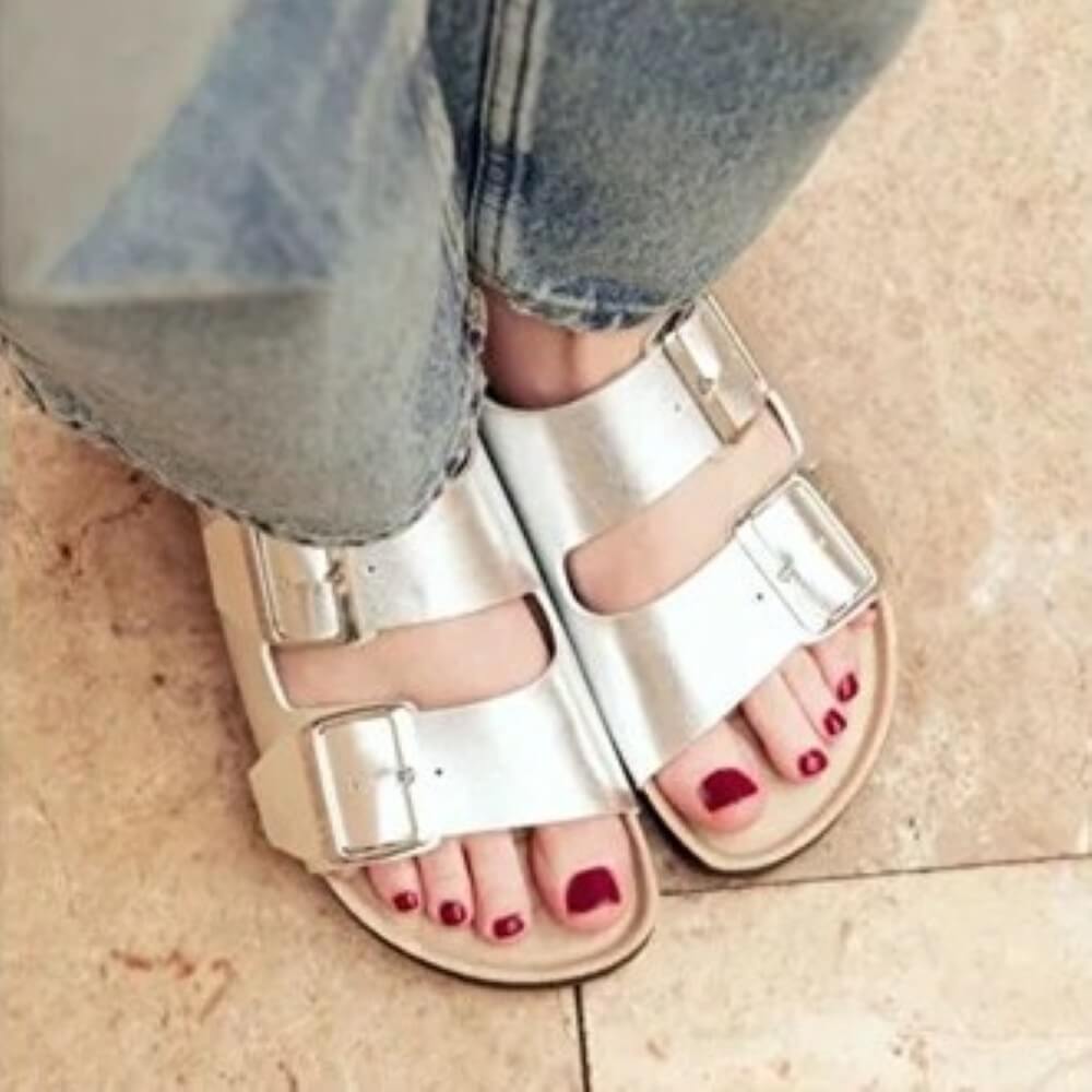 Genuins Silver sandals worn with denim jeans on a tiled floor.
