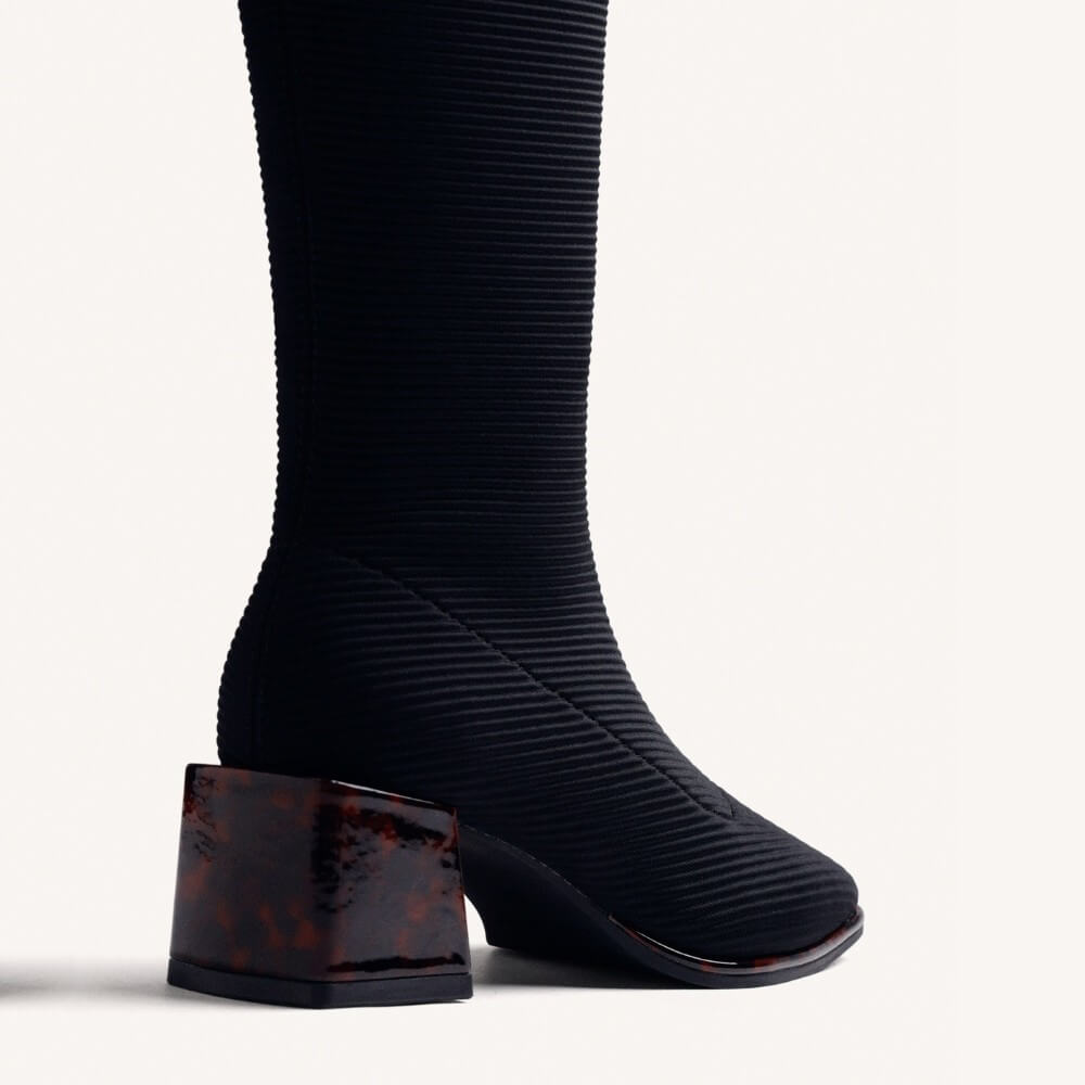 A Gioseppo  black ribbed knee-high boot with a pointed toe and a dark brown tortoiseshell block heel, shown in profile against a light grey background.