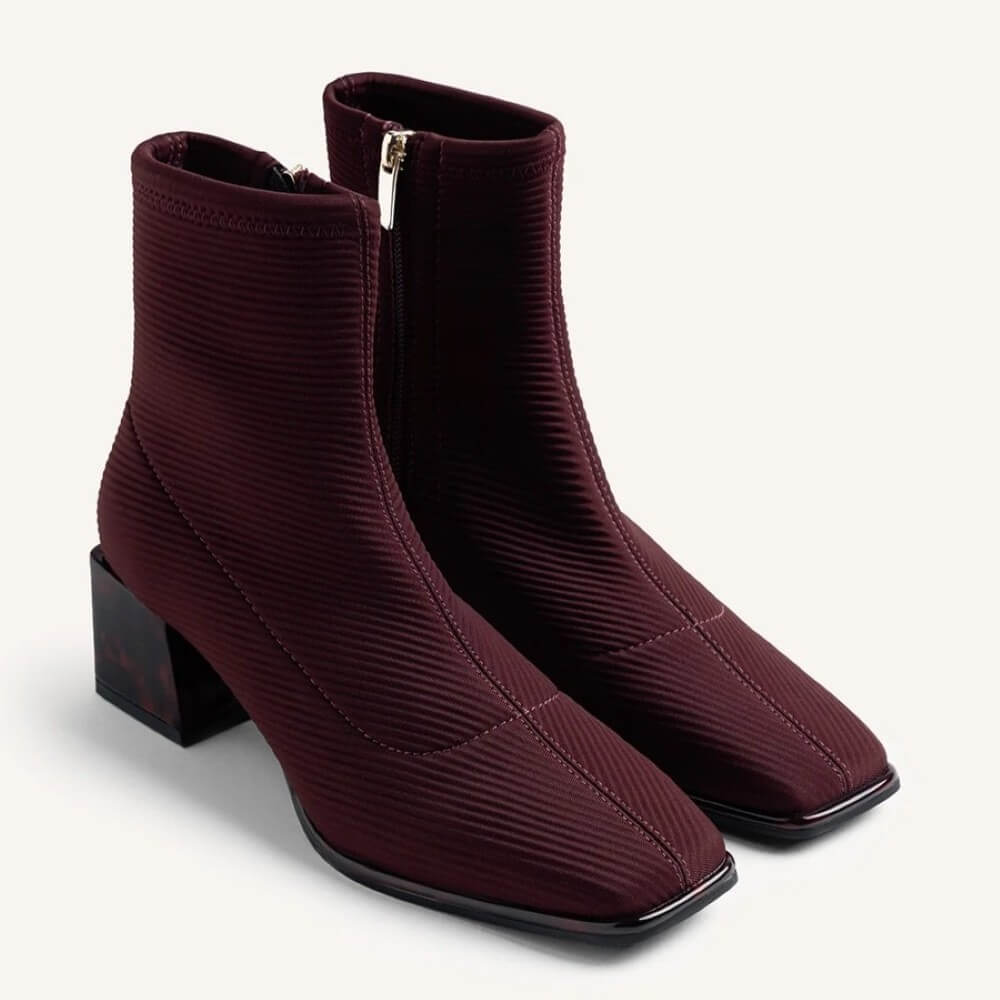 A pair of burgundy ribbed ankle boots with square toes and low block heels, shown on a light off-white background.