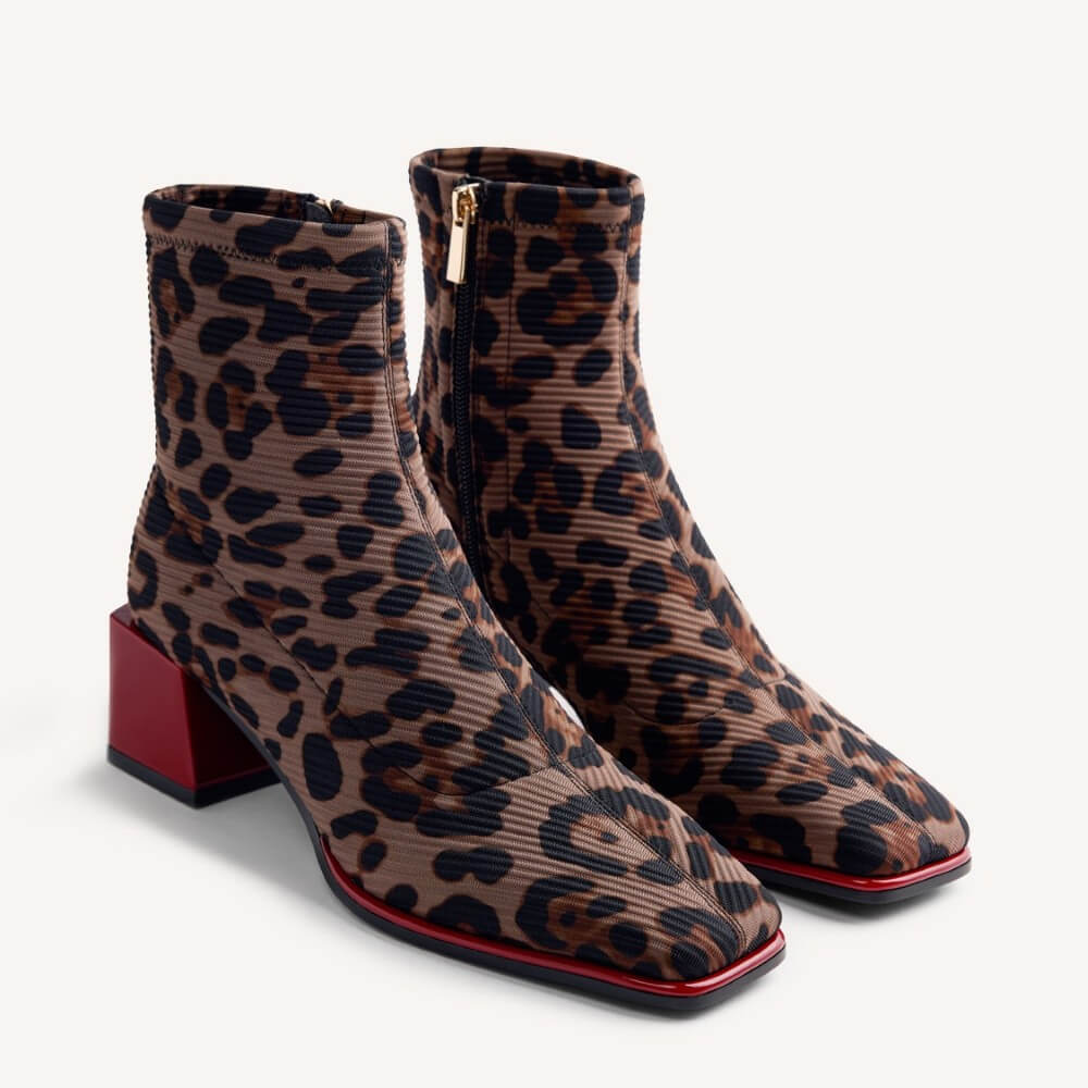 A pair of leopard-print ankle boots with a ribbed texture, square toes, and red block heels, shown on a light gray background.