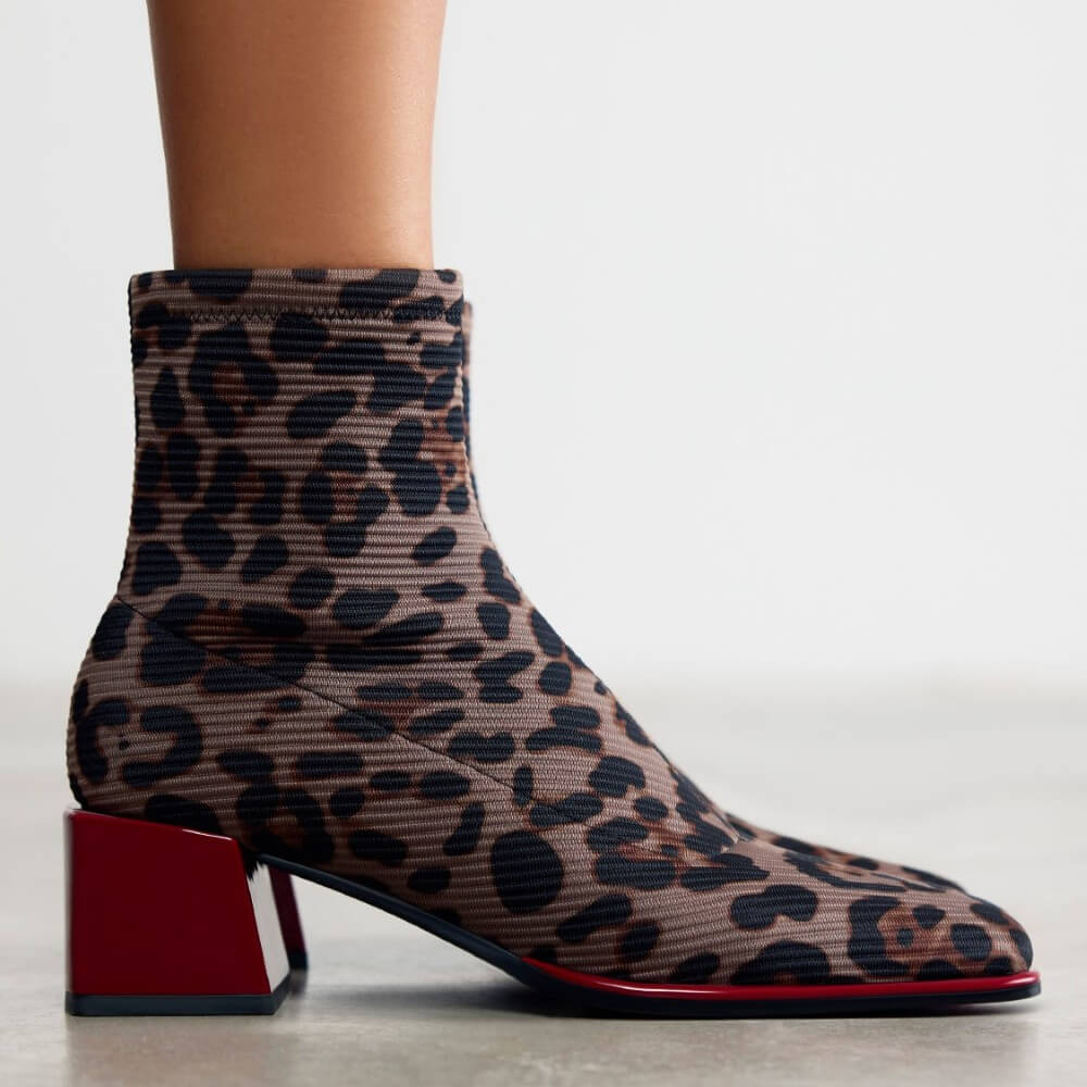 A Gioseppo ribbed ankle boot with a brown, black, and beige leopard print pattern and a bold red block heel, shown on a model's foot against a light grey background.