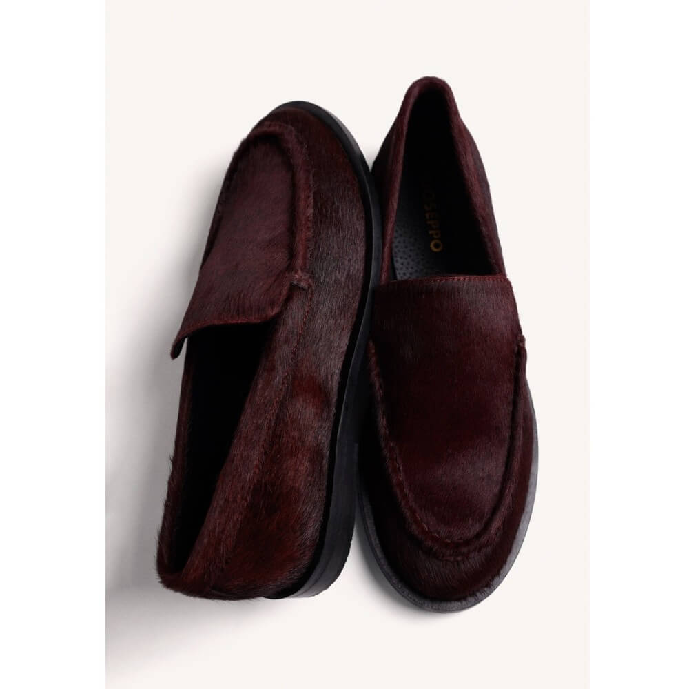 A pair of Gioseppo dark burgundy slip-on loafers with a textured hair-on-hide finish, displayed on a clean off-white background.