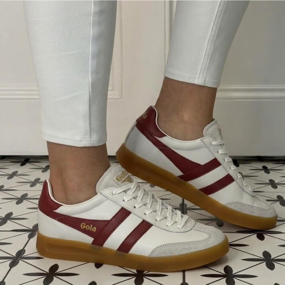 Gola White sneakers with red stripes and brown soles worn by a person on a patterned floor.