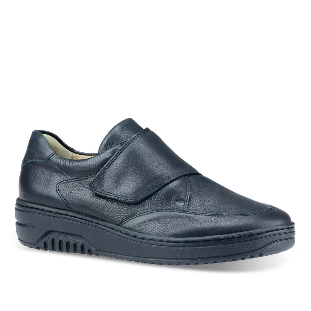 A Hartjes Black slip-on leather shoe with a Velcro strap and a thick, ridged sole, shown from a three-quarters angle on a white background.