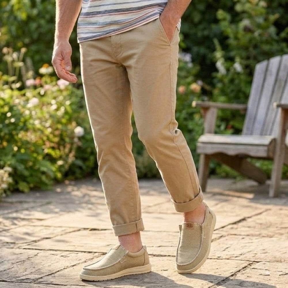 Person wearing beige pants and shoes standing on a patio with garden background