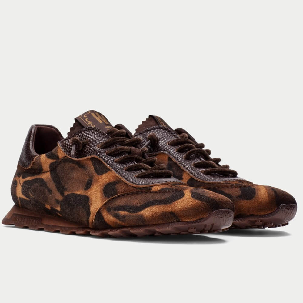 A pair of Hispanitas low-top sneakers featuring a brown and black animal print pattern, with dark brown laces and a dark brown sole, shown against a light grey background.