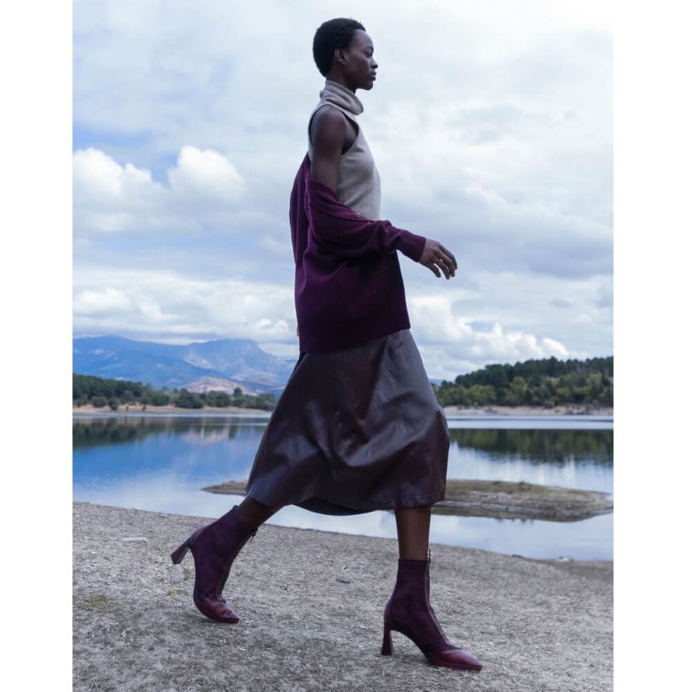 Woman walking by a lake with mountains in the background wearing wine boots