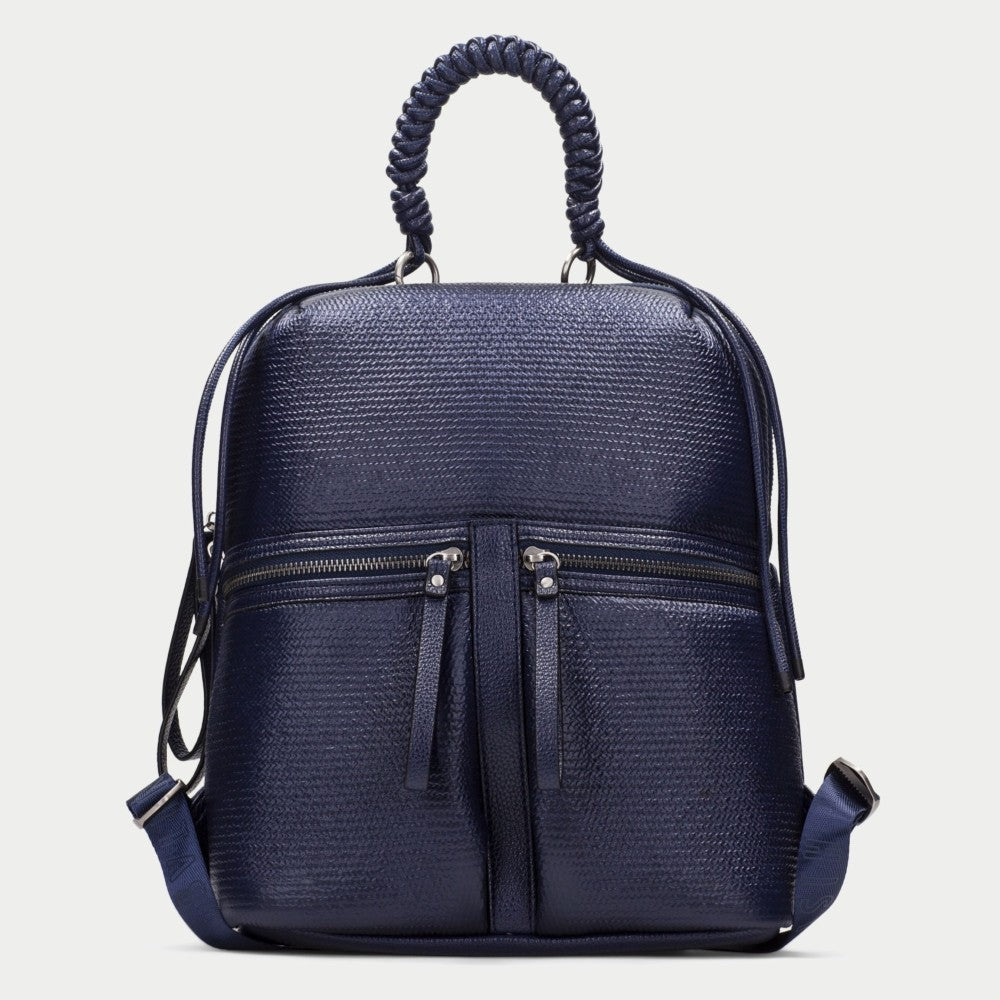 A Hispanitas navy blue textured backpack with a braided top handle, dual front zippered pockets, and a detachable shoulder strap, shown against a light grey background.
