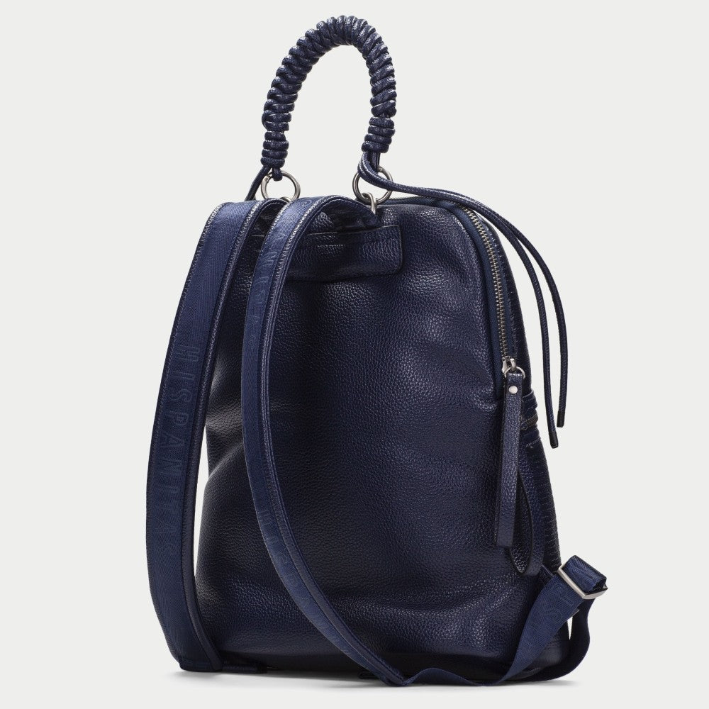 A Hispanitas navy blue textured backpack with a braided top handle, dual front zippered pockets, and a detachable shoulder strap, shown against a light grey background.