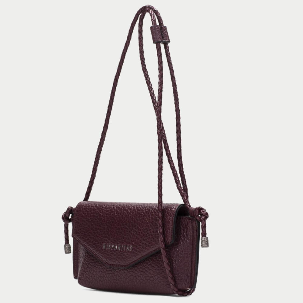 A burgundy pebbled PU leather clutch bag with a flap closure and braided strap details, featuring the brand name 'HISPANITAS' in silver lettering on the front, set against a plain light gray background.