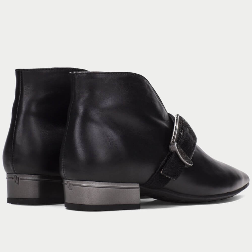 A pair of Hispanitas black leather ankle boots with a pointed toe and a wide strap across the instep featuring a silver-tone buckle, shown against a light gray background.