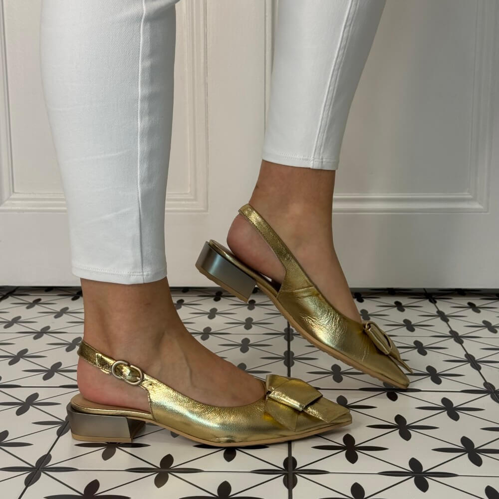 Hispanitas Platino Gold slingback shoes worn with white pants on a patterned floor.