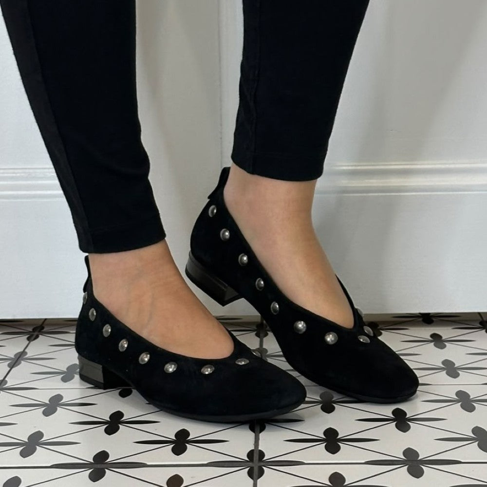 Hispanitas Black suede ballet flats with silver stud embellishments, shown on a model wearing black pants on a black and white patterned tile floor.