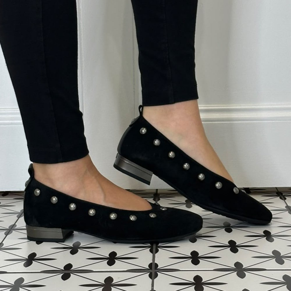 Hispanitas Black suede ballet flats with silver stud embellishments, shown on a model wearing black pants on a black and white patterned tile floor.