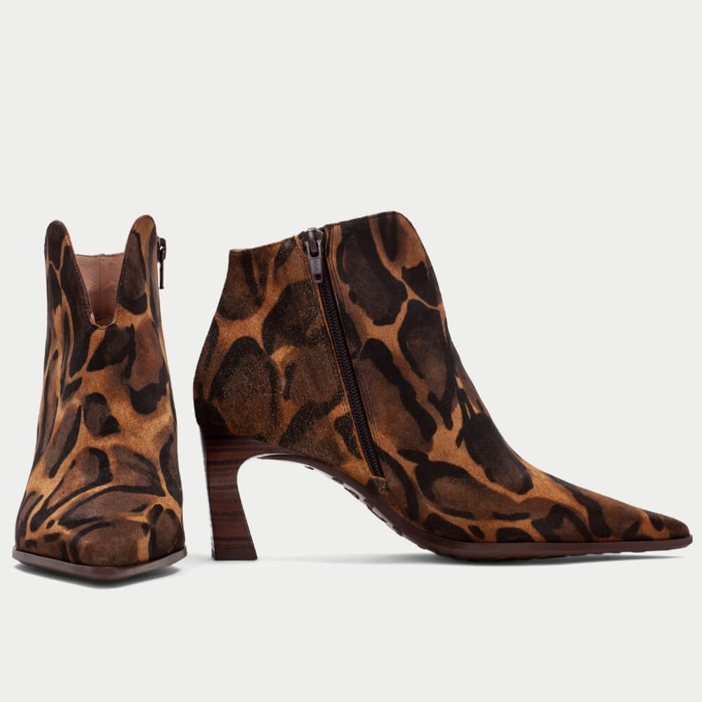 A pair of Hispanitas pointed-toe ankle boots with a brown and black Giraffe print pattern, featuring a mid-height wooden-look heel and a side zipper, shown against a light grey background.