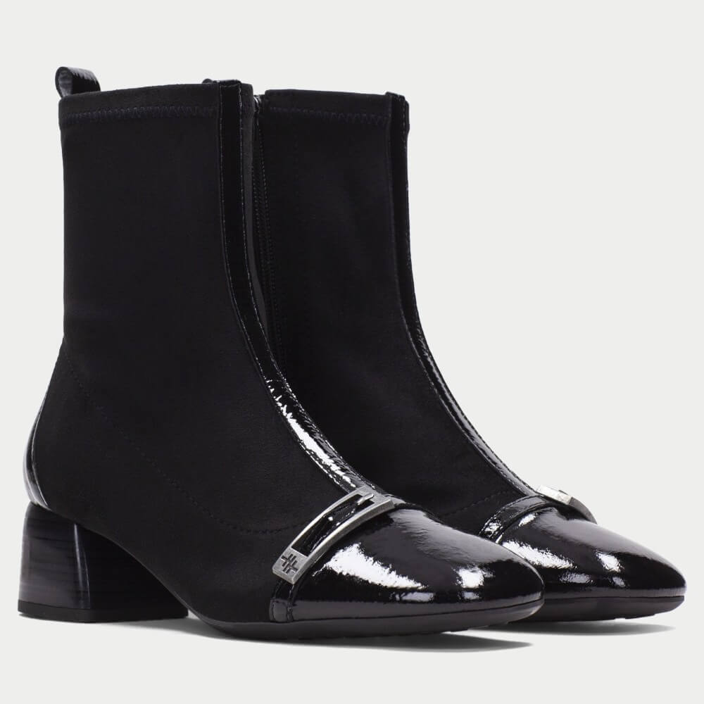 A pair of Hispanitas black ankle boots with a black elastic side gore, a low block heel, and a glossy patent leather toe cap featuring a silver-tone decorative buckle.