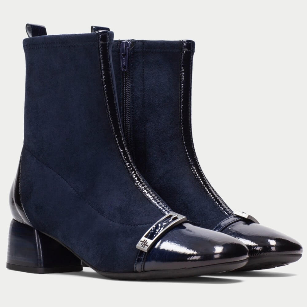 A pair of Hispanitas navy blue ankle boots with a mix of matte suede and glossy patent leather panels, featuring a low block heel and a decorative silver-tone metal band on the toe.