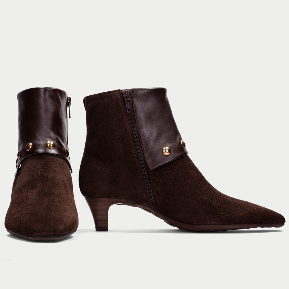 A pair of Hispanitas dark brown suede and leather ankle boots with a pointed toe, a stacked wooden-look heel, and a wide leather cuff embellished with gold-tone studs, shown against a light grey background.