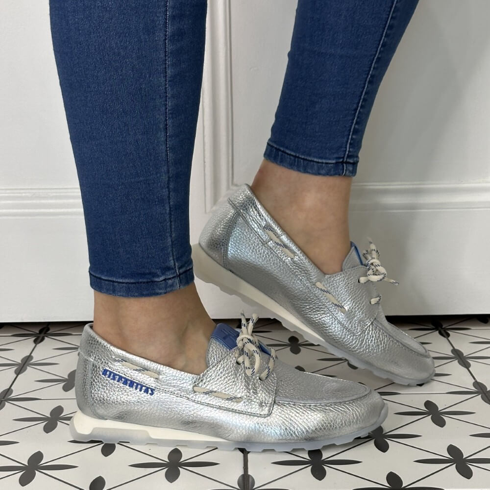 Silver loafers worn with blue jeans on a patterned floor.