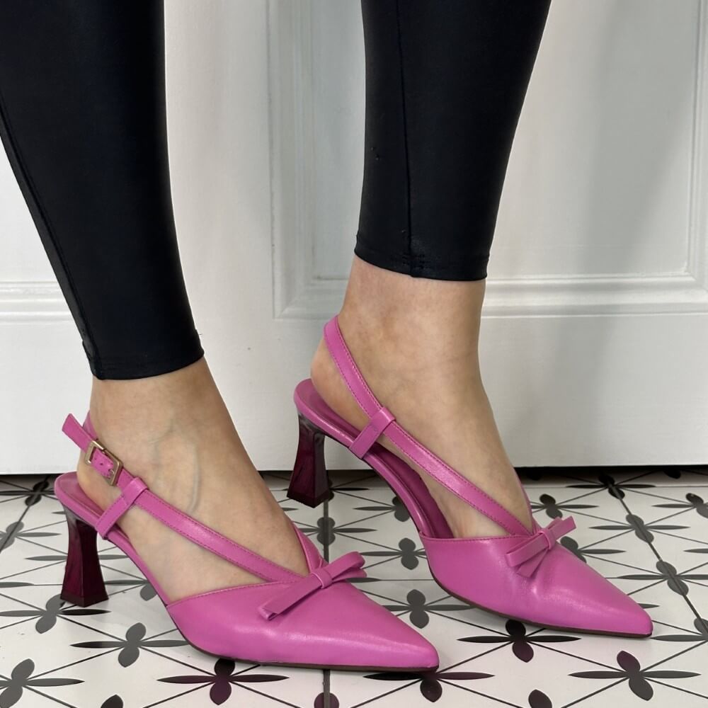 Pink high-heeled shoes with bow details worn by a person on a patterned floor.