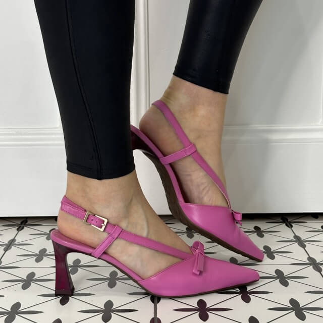 Pink high-heeled shoes worn with black pants on a patterned floor.