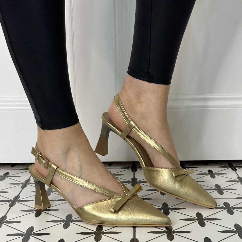 Gold high-heeled shoes worn with black leggings on a patterned floor.