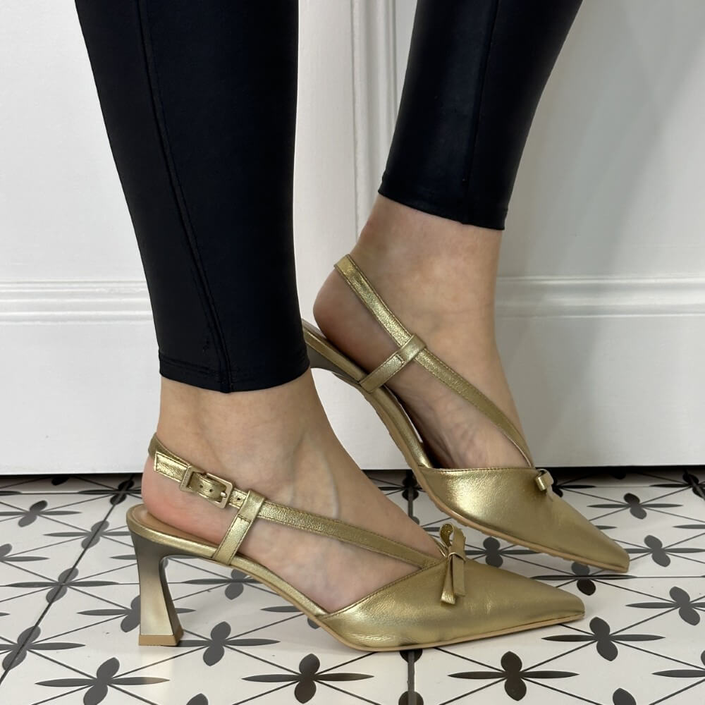Gold high-heeled shoes worn with black pants on a patterned floor.