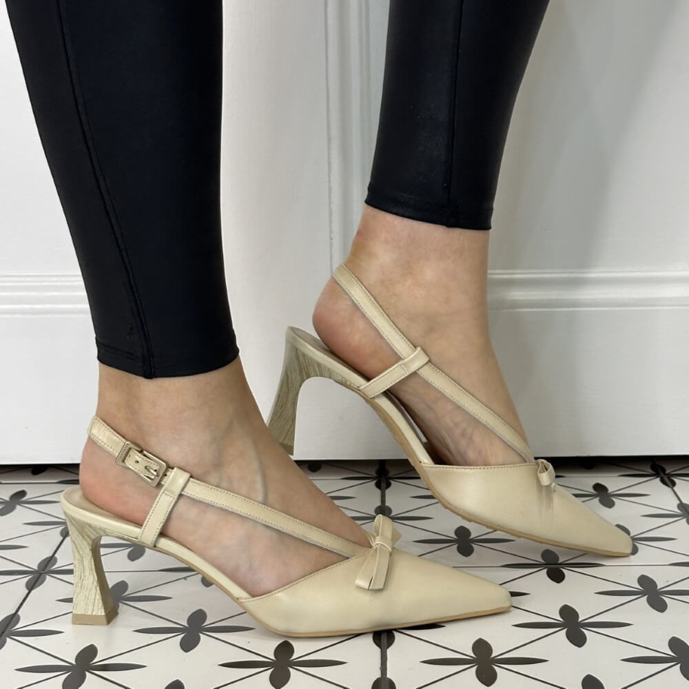 Beige high-heeled shoes worn with black pants on a patterned floor.