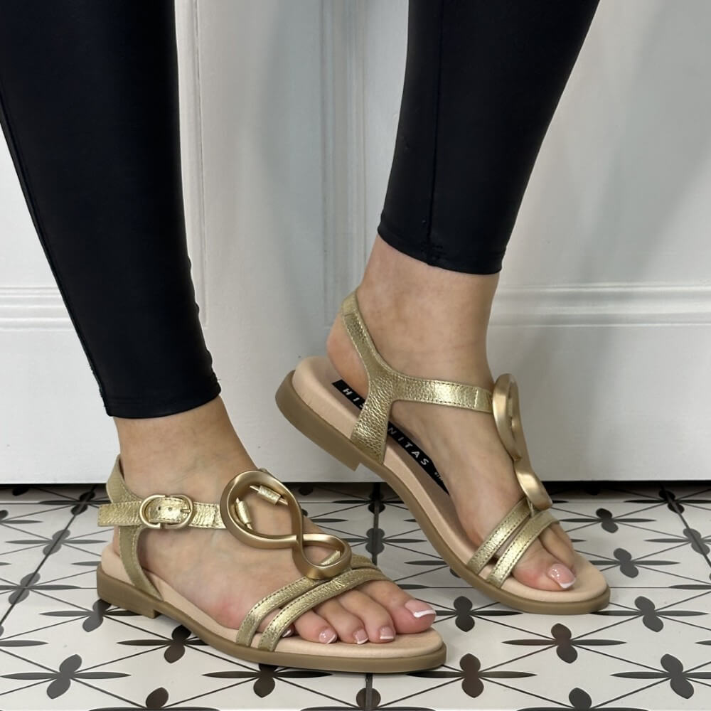 Gold sandals worn with black leggings on a patterned floor.