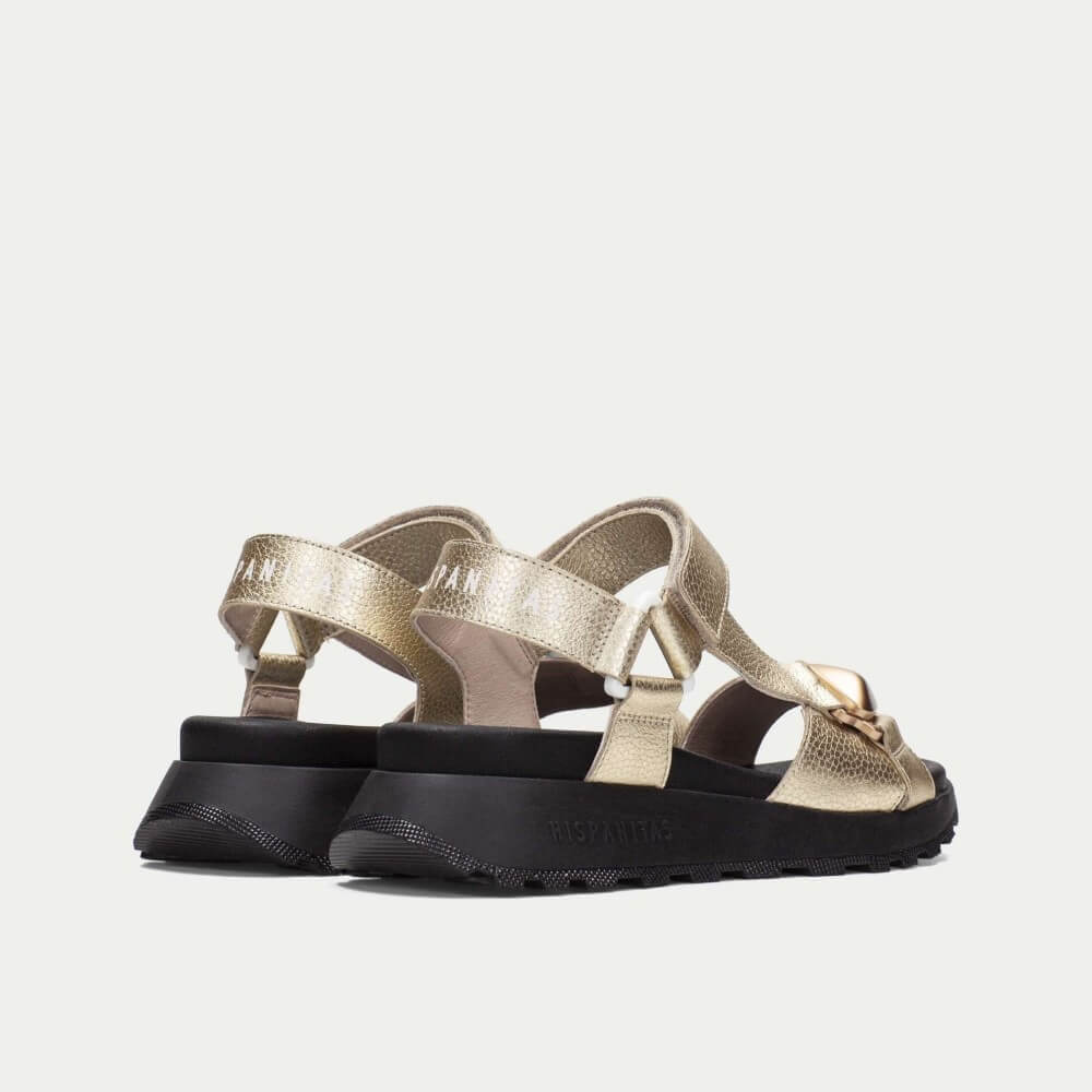 Gold sandals with black soles on a white background