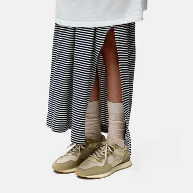 Person wearing a striped skirt, white shirt, beige socks, and Hoff sneakers on a light background