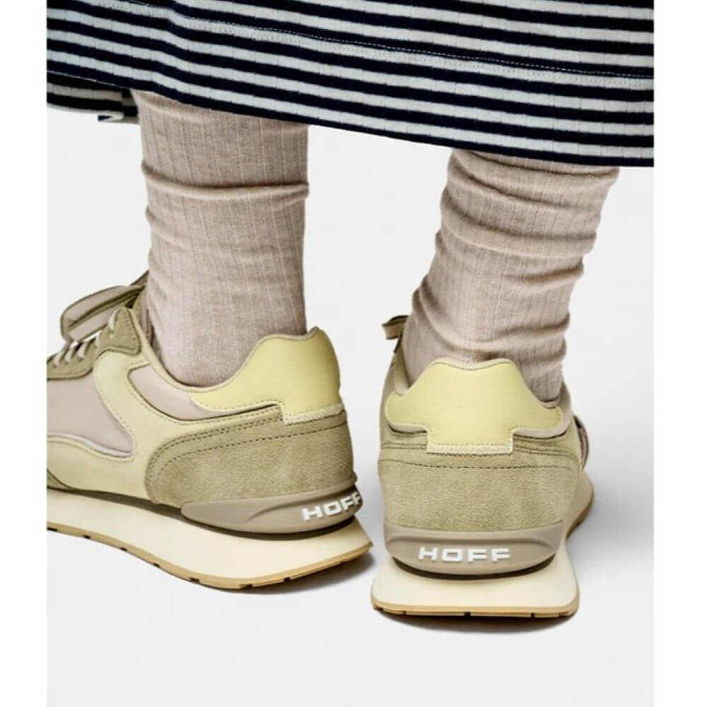 Beige sneakers with 'HOFF' branding worn by a person in striped pants and beige socks.