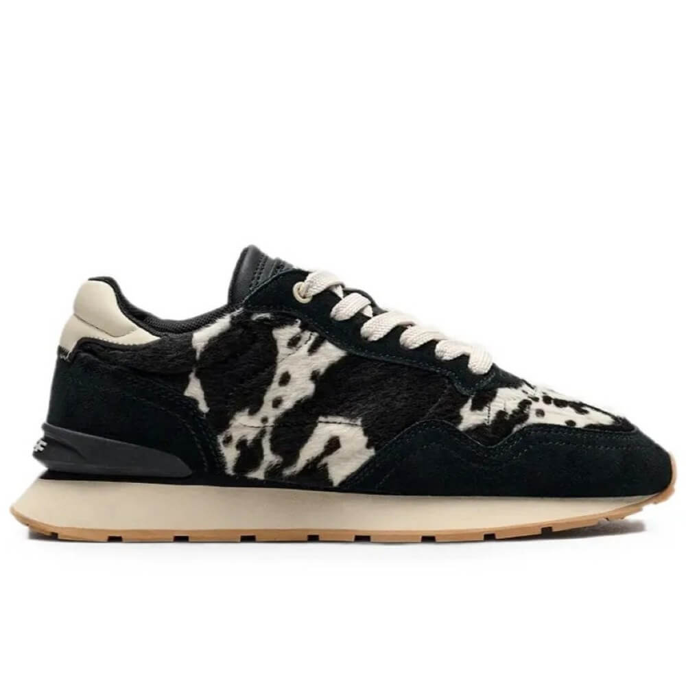 A Hoff low-top sneaker featuring a black and cream cow-print pattern on the upper, black laces, a cream heel tab, and a thick cream midsole with a gum outsole.