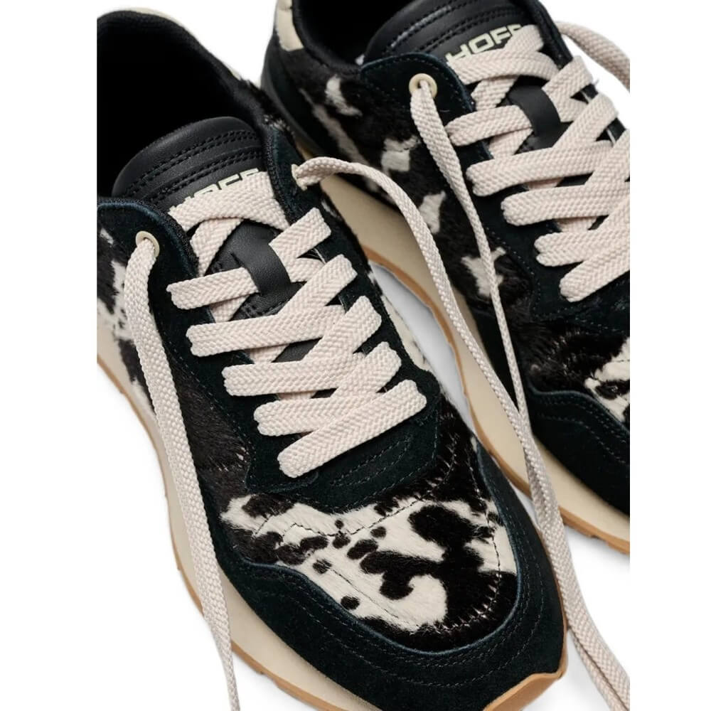 A pair of Hoff low-top sneakers with a black and off-white cow-print pattern, featuring off-white laces and beige midsoles on a white background.